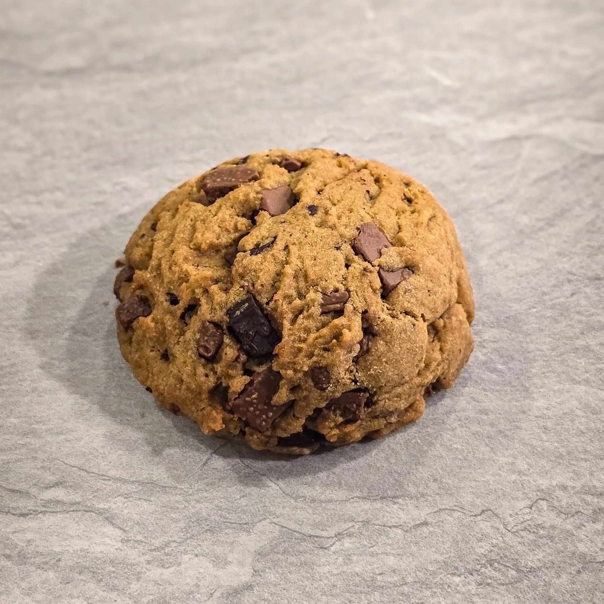 A thick cookie studded with milk and dark chocolate chunks, on a stone counter