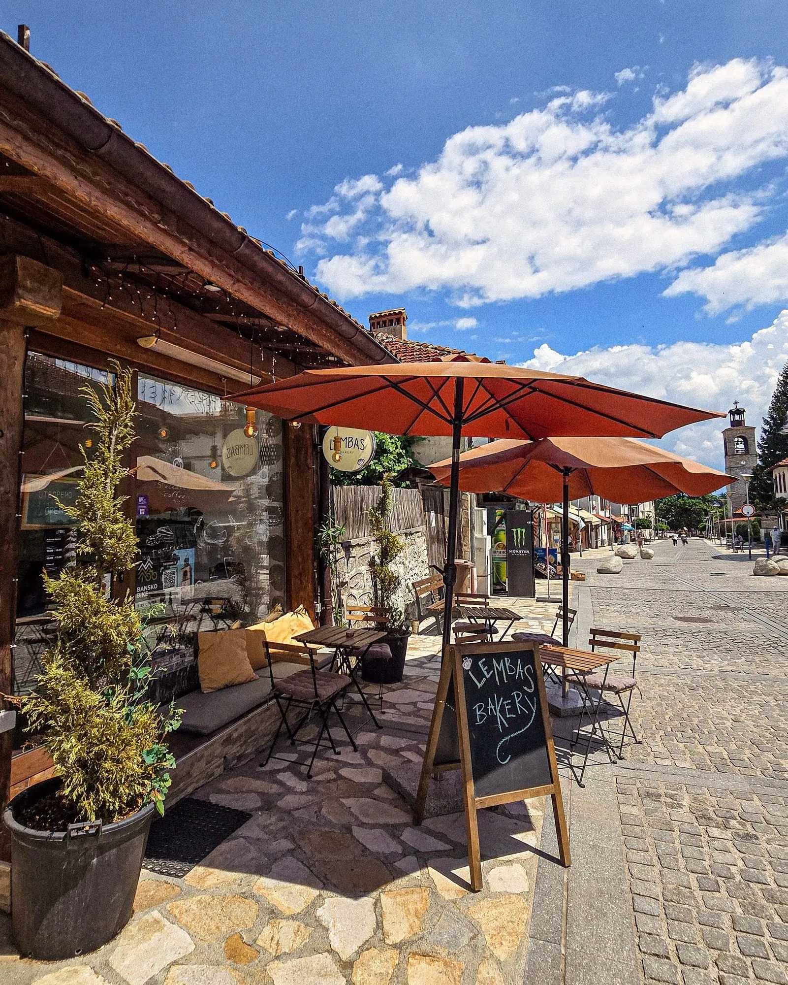 The Lembas storefront on Pirin Street, terracotta parasols over the outdoor tables and the Bansko clock tower down the cobbles